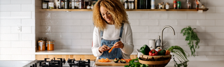 Anti Aging Nutrition Tips: a young woman with curly  hair in denim overalls prepares  vegetables in a sunny kitchen.