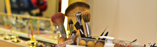 Makeup brushes stored in a vanity organizer in a bright room, surrounded by makeup and hair products.
