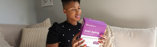 An African-American woman smiles as she reads the label of her VitaMedica Anti-Aging Formula box.
