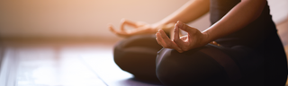 A woman is sitting cross-legged with her hands on her knees to practice mindful meditation. 