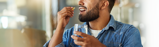 Man with beard in chambray shirt taking vitamins with a glass of water. 