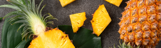 A brightly-colored yellow, green, and brown pineapple is sliced in half on a black stone countertop. 