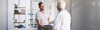 A smiling young man receives surgical advice from his doctor in a modern, brightly-lit medical office.