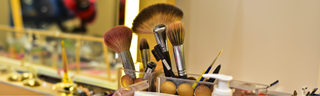 Makeup brushes stored in a vanity organizer in a bright room, surrounded by makeup and hair products. 