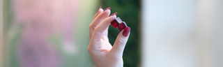 A woman's hand with long red nails hold blackberry flavored gummy vitamins up in the light