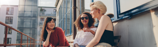 Three women site together in the sun on a city rooftop. 