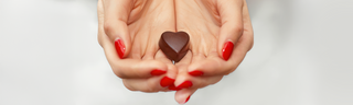 A woman with red nails holds a heart-shaped piece of chocolate in her hands