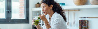 Woman drinking a green gut health smoothie in a bright kitchen for