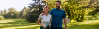 A smiling caucasian couple walks through the park in athletic clothing after their morning jog. 