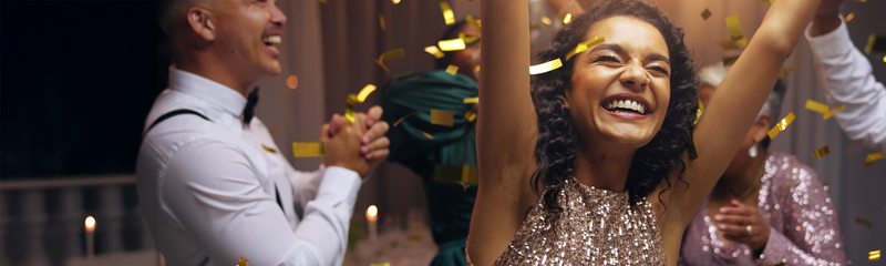 A healthy, happy man and woman celebrate the new year in party clothes. Confetti is being thrown into the air. 