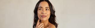 A woman in her early 40s with shoulder-length brown hair and glowing skin holds her hand to her face. 