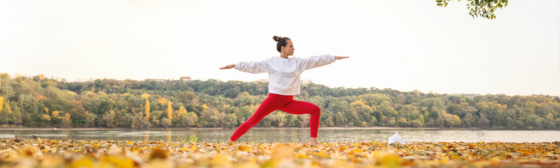 A woman in a white sweatshirt and red leggings exercises in a beautiful, outdoor Fall setting. 